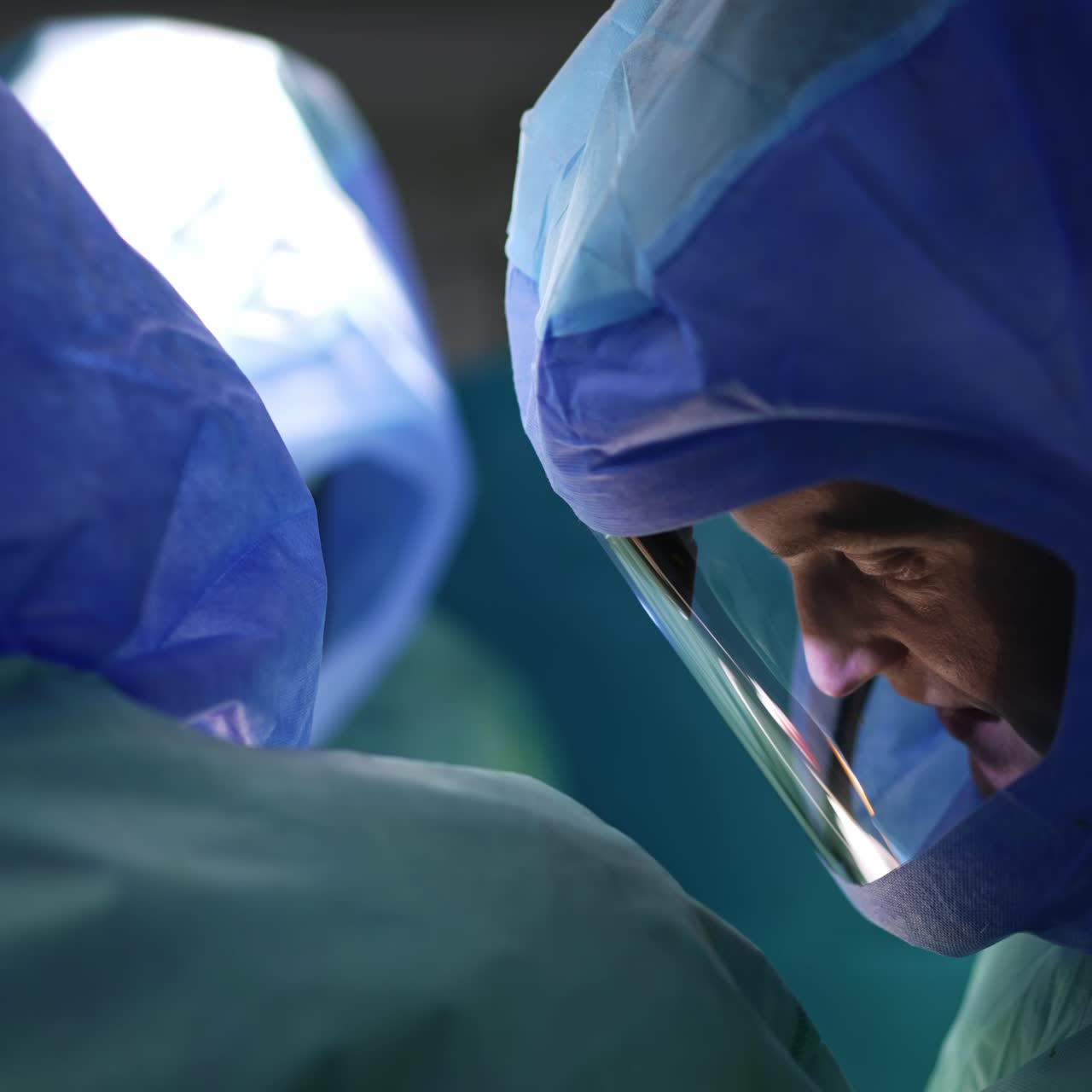 Male doctor wearing protective helmet looking down at patient. Surgeon cooperating in the surgical team at operation