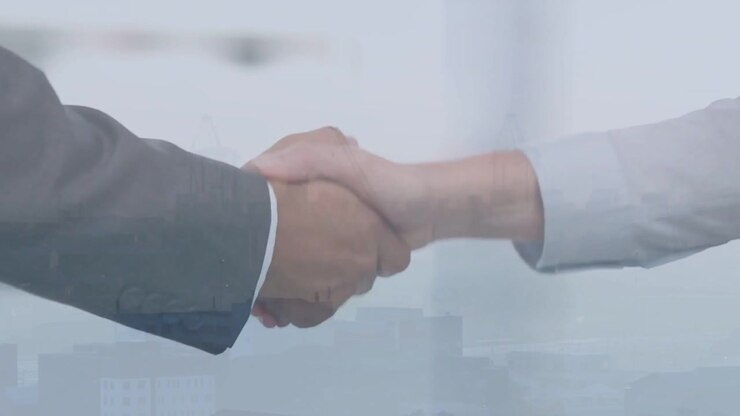Gli avambracci di due professionisti che si stringono la mano in una scena d'affari, con un overlay di skyline che sigilla l'accordo.