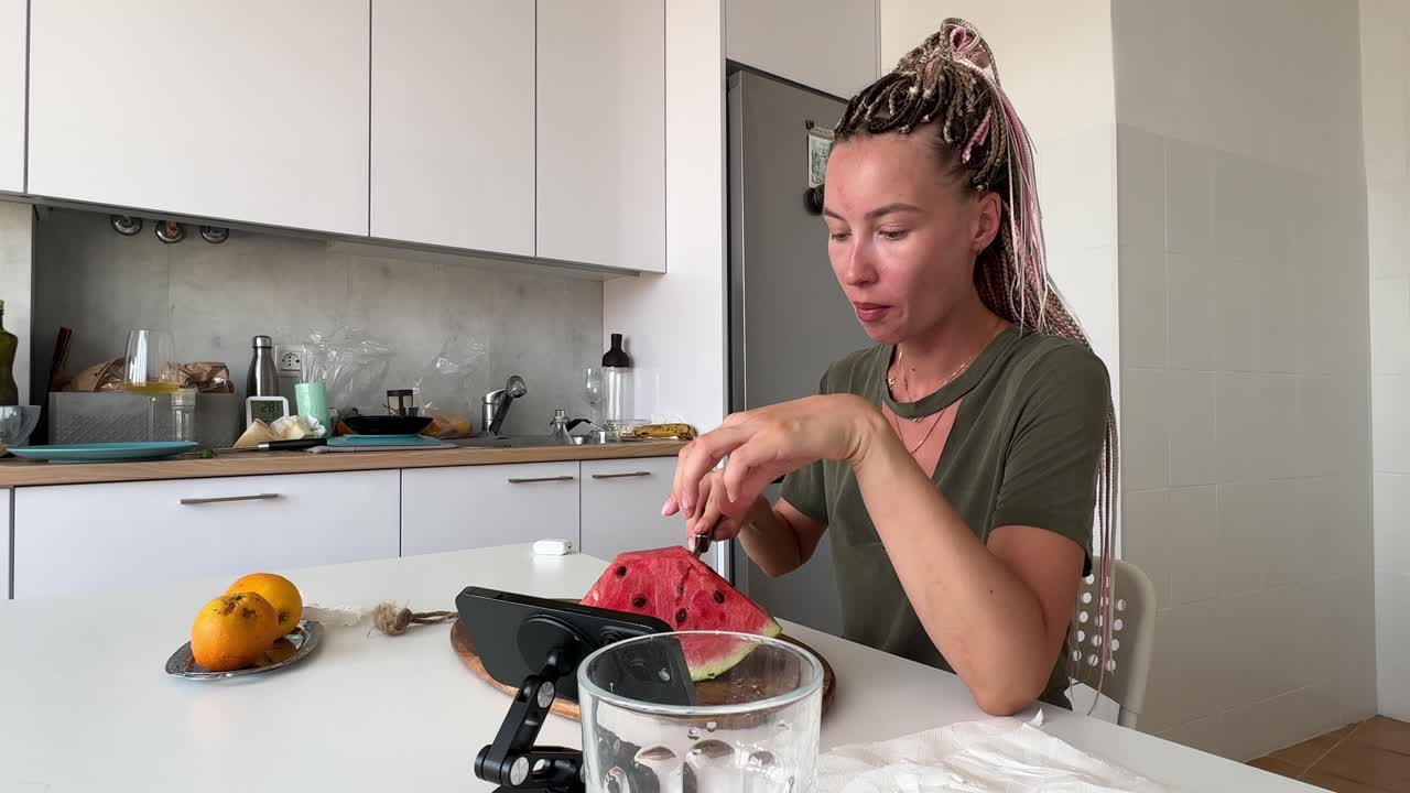 Giovane donna che taglia e mangia anguria in una cucina moderna.
