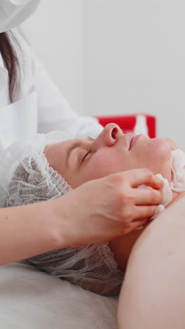 cosmetologist doctor wipes woman face and neck cleaning procedure with cotton pads in beauty clinic