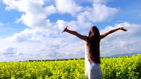 young woman with arms outstretched standing in field