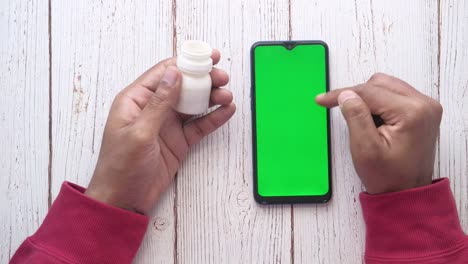 persona sosteniendo un frasco de medicina y un teléfono inteligente con una pantalla verde
