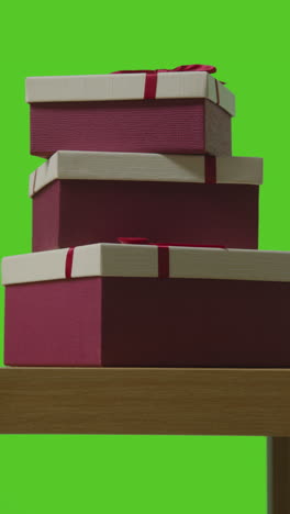 vertical video of pile of presents in gift wrapped boxes on table shot against green screen