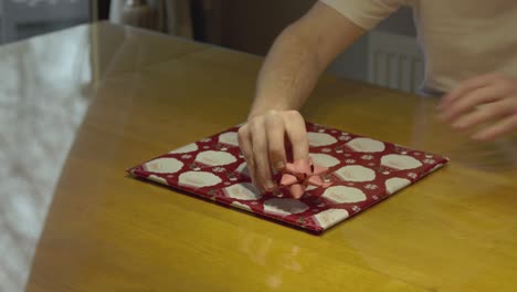 Statische-Aufnahme-Von-Händen,-Die-Eine-Schleife-Auf-Ein-Verpacktes-Weihnachtsgeschenk-Aus-Vinyl-Anbringen