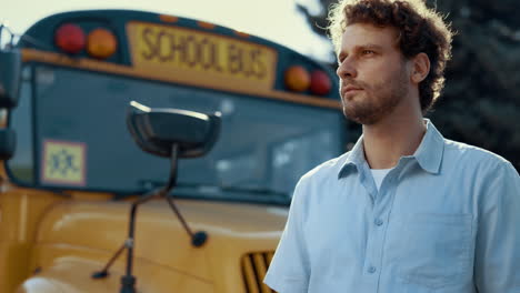 portrait car driver stand near yellow school bus. serious man looking camera.