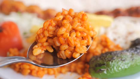 close-up of bulgur pilaf on a spoon with other dishes in background