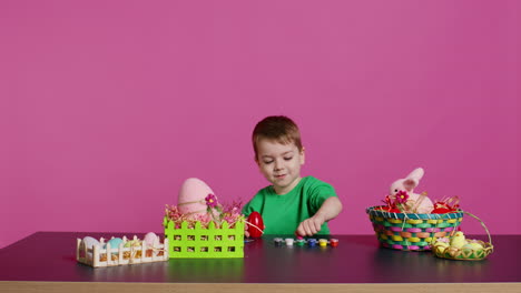 ecstatic little kid using watercolor and paintbrushes to decorate eggs