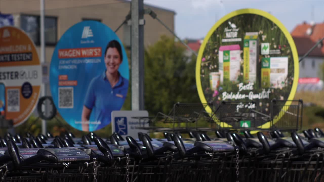 A stack of supermarket metal trolleys for goods transport, lined up in front of the market entrance. Perfect for themes of retail logistics, goods handling, and market operations.