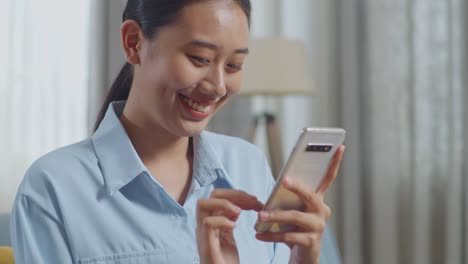 Close Up Of Asian Woman Enjoys Using Smartphone While Sitting On Sofa In The Living Room