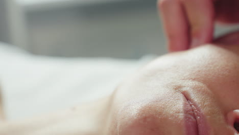 professional cradles customer jawline to ear side with gentle fingertips during soothing facial massage under soft clinical lighting beside subtle product trolley for relaxing spa experience