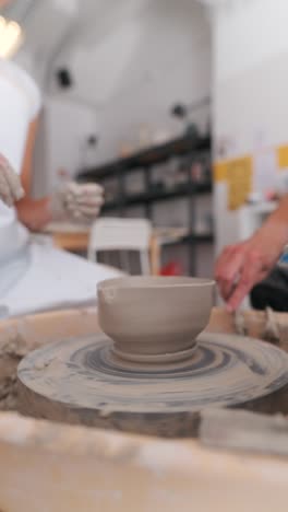 a close-up of a clay pot being shaped on a pottery wheel in a studio