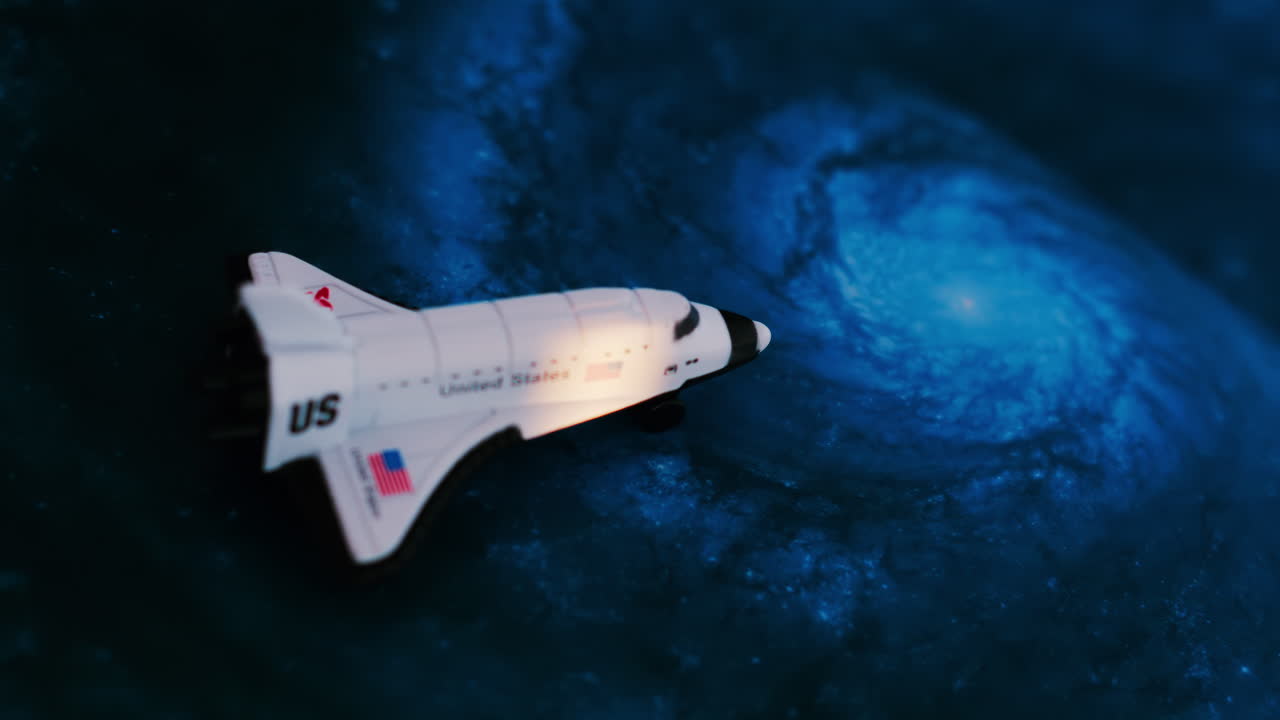 Close up of a miniature toy space shuttle placed on a blue cosmic galaxy backdrop