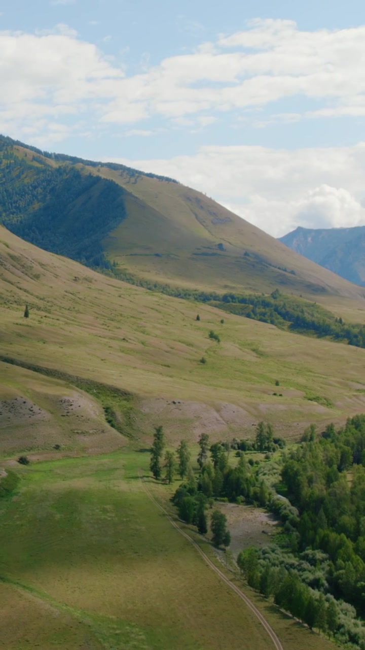 Filmato panoramico della Valle di Ak-Kem sui Monti Altai, Russia, con dolci colline verdi, pendii boscosi e una piccola baita rurale sotto un cielo nuvoloso.