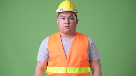 젊은 잘생긴 과체중 아시아인 남자 건설 노동자 초록색 배경