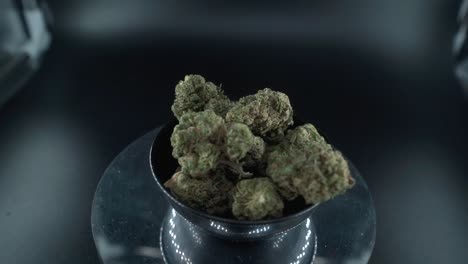 brotes de marihuana secos verdes disparado de cerca, montón de plantas de marihuana secas en un cuenco brillante, cepas de tricomas, en un soporte giratorio reflectante, luces de estudio, zoom cinematográfico en cámara lenta 120 fps