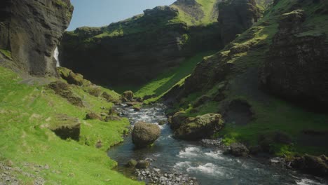 Kvernufoss-waterfall-and-the-river-below-in-Iceland,-sunny-green-rocks-and-rushing-water-in-the-foreground