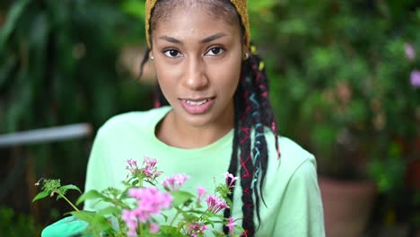 happy ethnic woman with potted flowers in hothouse