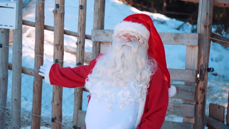 santa está de pie junto a una valla de madera y hablando con la cámara
