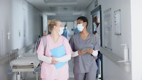 happy diverse female doctors wearing face masks talking and walking in corridor, slow motion