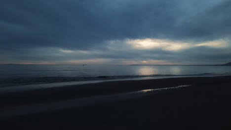 Vista-Oscura-De-La-Playa-Vacía-Con-Olas-Tranquilas-Y-Cielo-Dramático