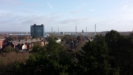 Aerial-view-over-park-trees-to-industrial-townscape-with-blue-skyscraper,-Merseyside,-England,-Dolly-right