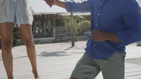 Happy-diverse-couple-in-sunglasses-stepping-into-pool-from-sunny-beach-deck,-in-slow-motion