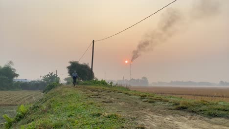 Runner-jogging-towards-camera-on-rural-road,-Gas-Plant-polluting-air-behind