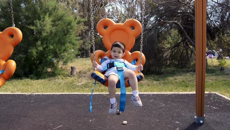 Niño-De-Dos-Años-Relajándose-En-Un-Columpio-Con-Forma-De-Oso-De-Peluche-En-El-Parque