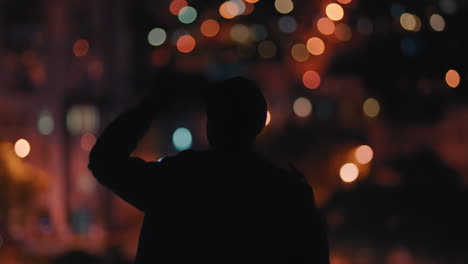 silhouette of man with arm raised on rooftop at night celebrating freedom achievement looking at beautiful city lights rear view