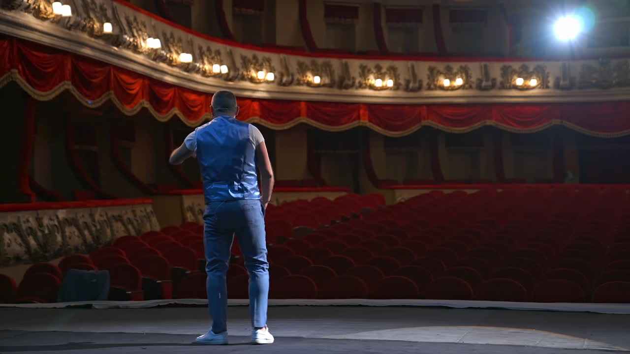 Actor on classic theatre stage. Man is speaking in spotlights during the performance. Back view video.