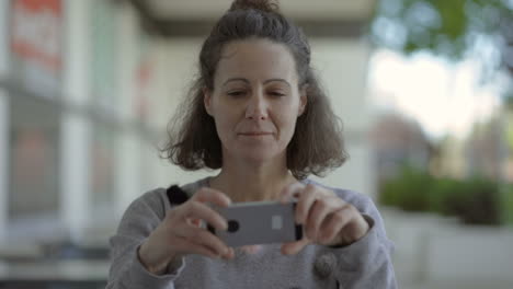 Smiling-mature-woman-holding-smartphone-in-outstretched-arms