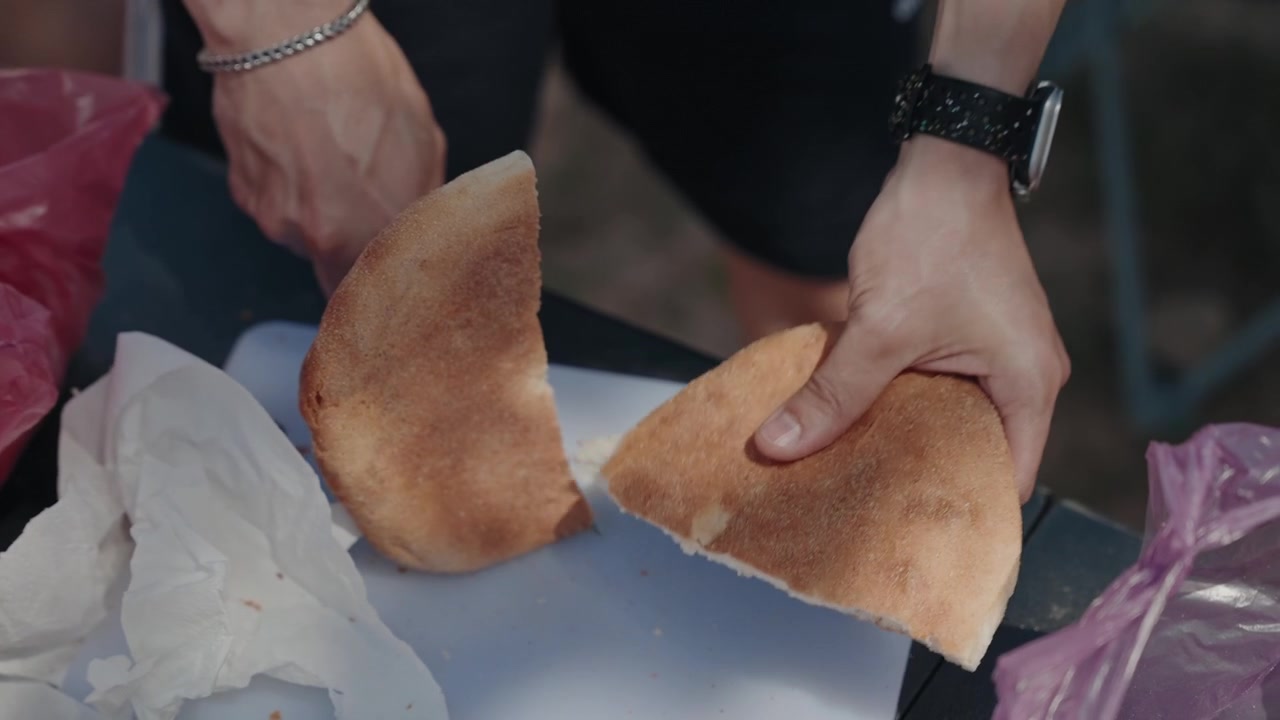 Hands cutting a round crusty bread loaf open with a knife on a white board