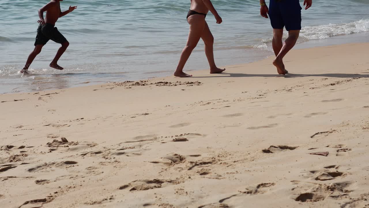 두 사람이 푸켓의 카론 해변의 모래 해변을 따라 밝은 낮에 산책하며 평온한 해변 순간을 포착합니다.