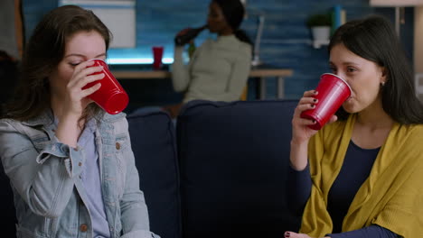 Two-women-relaxing-on-sofa-drinking-beer-while-socializing-during-home-party