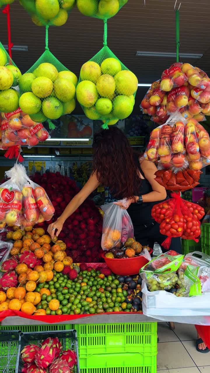 San José, Costa Rica, 4 de agosto de 2025: Mulher escolhendo frutas tropicais frescas em uma barraca de mercado local. Cliente feminina comprando em uma colorida barraca de frutas com pitaya e rambutãs