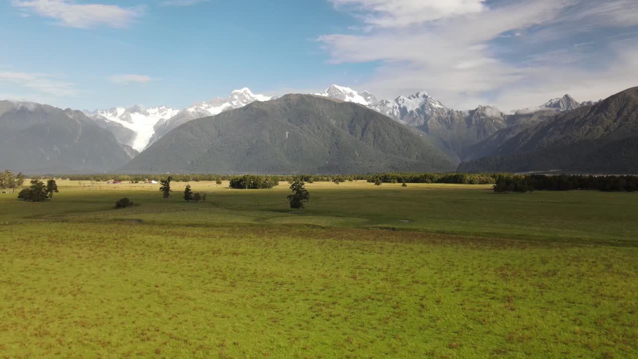 Suggestiva vista aerea panoramica di una massiccia catena montuosa e di terreni agricoli verdi in Nuova Zelanda - riprese in allontanamento con drone
