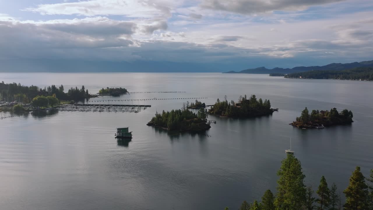 Kleine bewaldete Inseln verstreut über ruhigem Seewasser um einen Bootsanlegeplatz unter bewölktem Himmel, Flathead Lake Montana USA