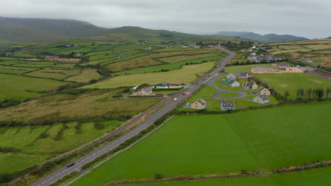 Luftpanoramaaufnahmen-Der-Landschaft-An-Bewölkten-Tagen.-Fahrzeuge,-Die-Auf-Einer-Stark-Befahrenen-Straße-Durch-Das-Dorf-Fahren.-Irland