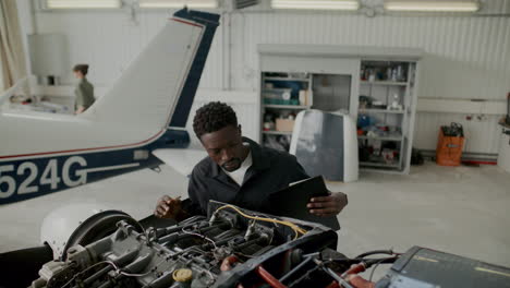Aircraft Inspector Examining Airplane Engine and Taking Notes in Hangar