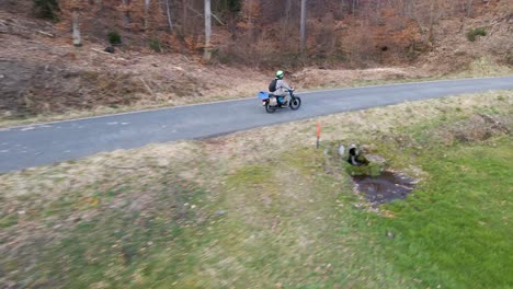 Aerial-footage-of-a-person-on-a-motorbike-driving-along-a-narrow-forest-road