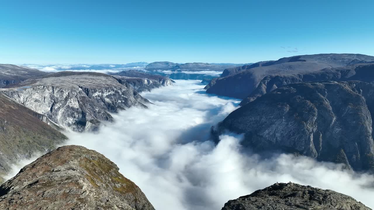Il drone si allontana e sale sopra Bakkanosi, rivelando il fiordo e uno splendido paesaggio montano sotto un cielo blu