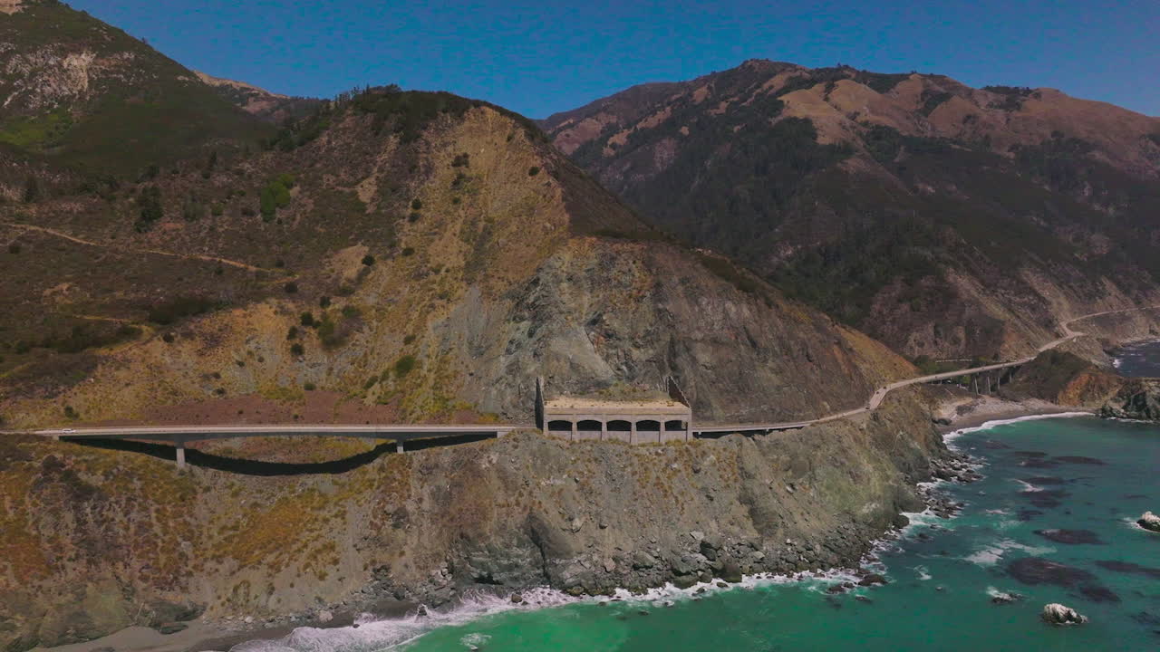 Road connecting the mountains at the coastline of California. Beautiful sight of the rugged rocks at the backdrop of blue clear sky.