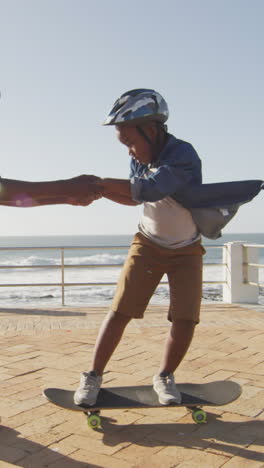 video of happy african american father learning son how to skateboard on promenade