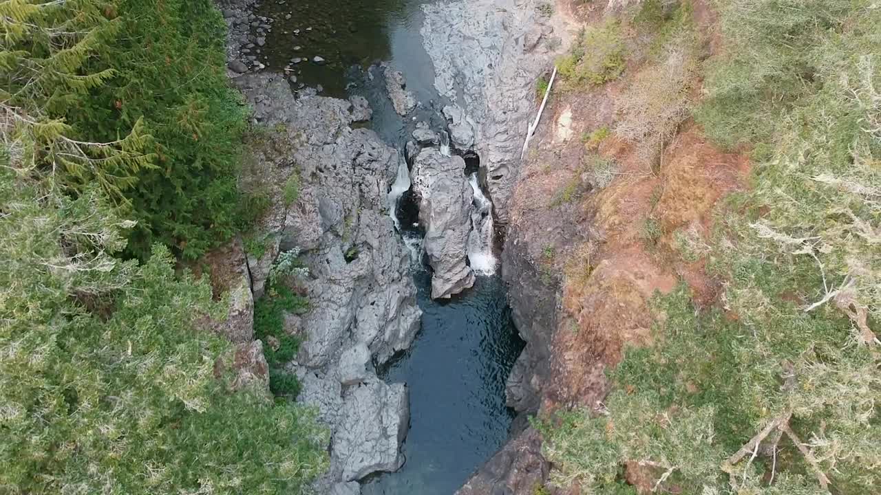dron panorámico hacia abajo de un río que fluye a través de un valle que se divide en dos pequeñas cascadas en la selva tropical de la columbia británica, canadá