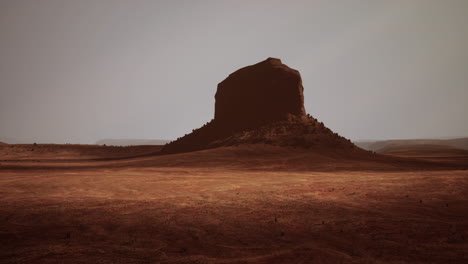 a lone red rock formation stands tall in the desert landscape of monument valley