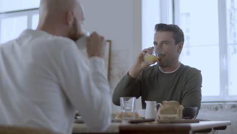 gay couple sitting at table, having breakfast and talking