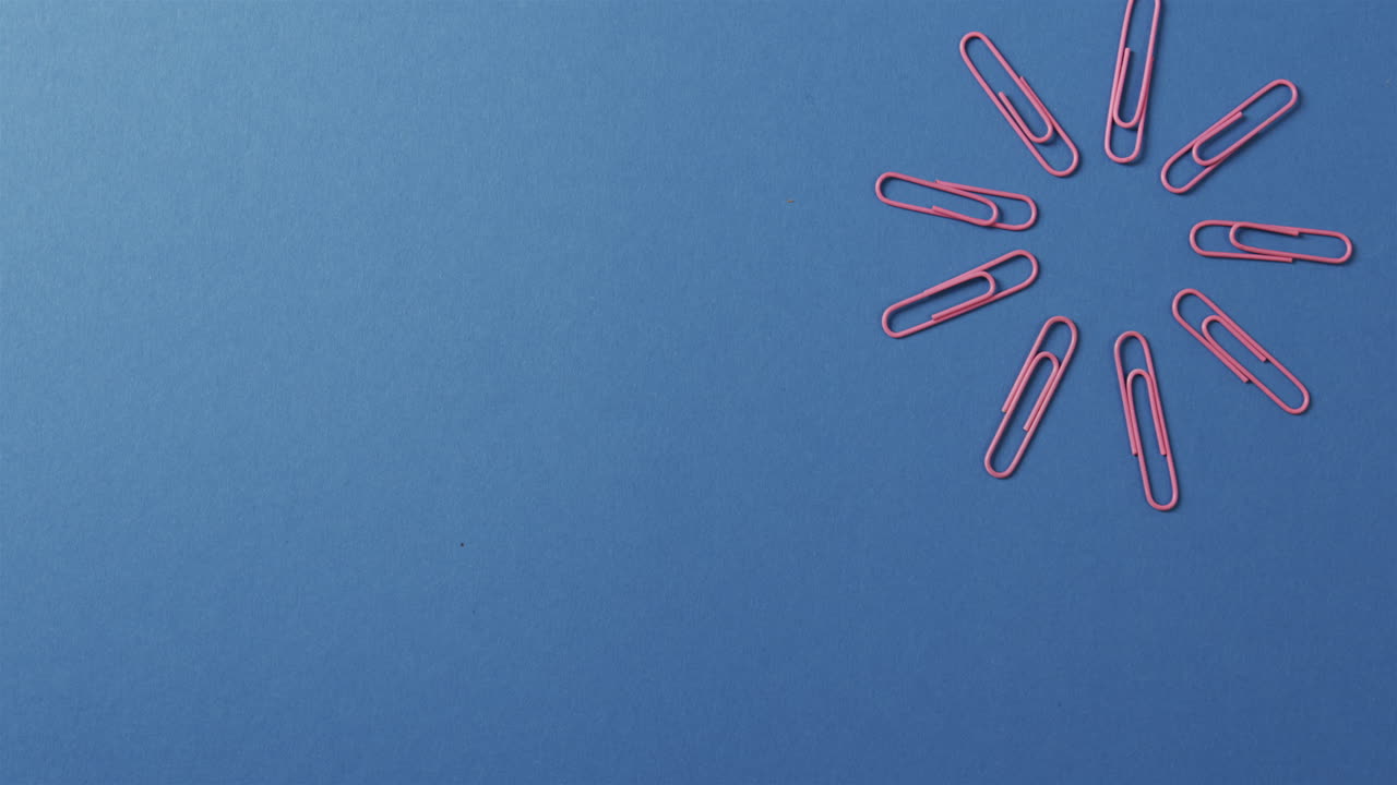 los clips de papel rosados están dispuestos en un patrón circular sobre un fondo azul, con espacio para copiar