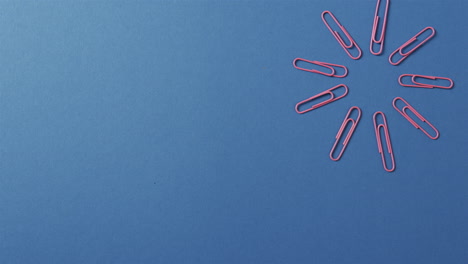 pink paper clips are arranged in a circular pattern on a blue background, with copy space