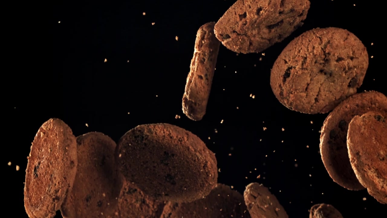 Biscotti con gocce di cioccolato che cadono al rallentatore su sfondo nero