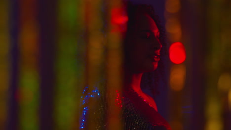 young woman having fun in nightclub or bar shot through tinsel curtain in foreground